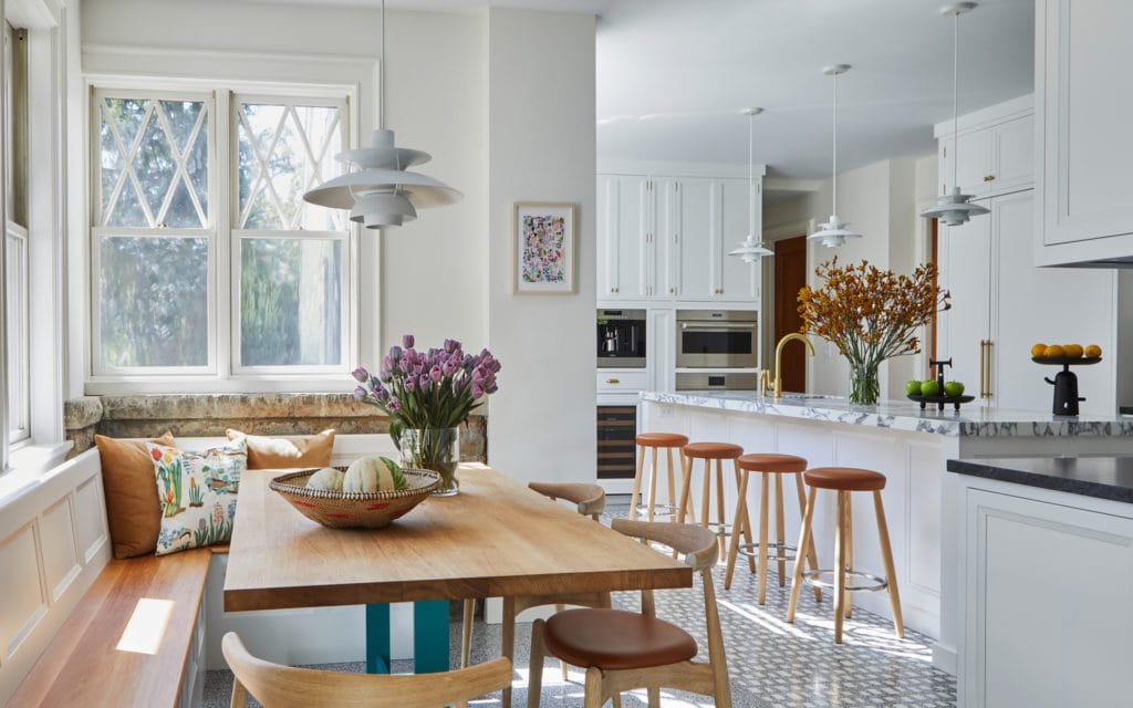 Inviting classic kitchen features white Bilotta cabinetry, custom banquette, sunlit windows and contemporary accents.