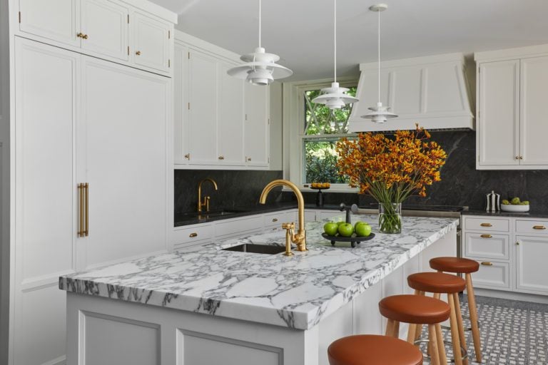 Classic kitchen features white Bilotta cabinetry with gold accents, custom island with marble top and contemporary pendant lights.