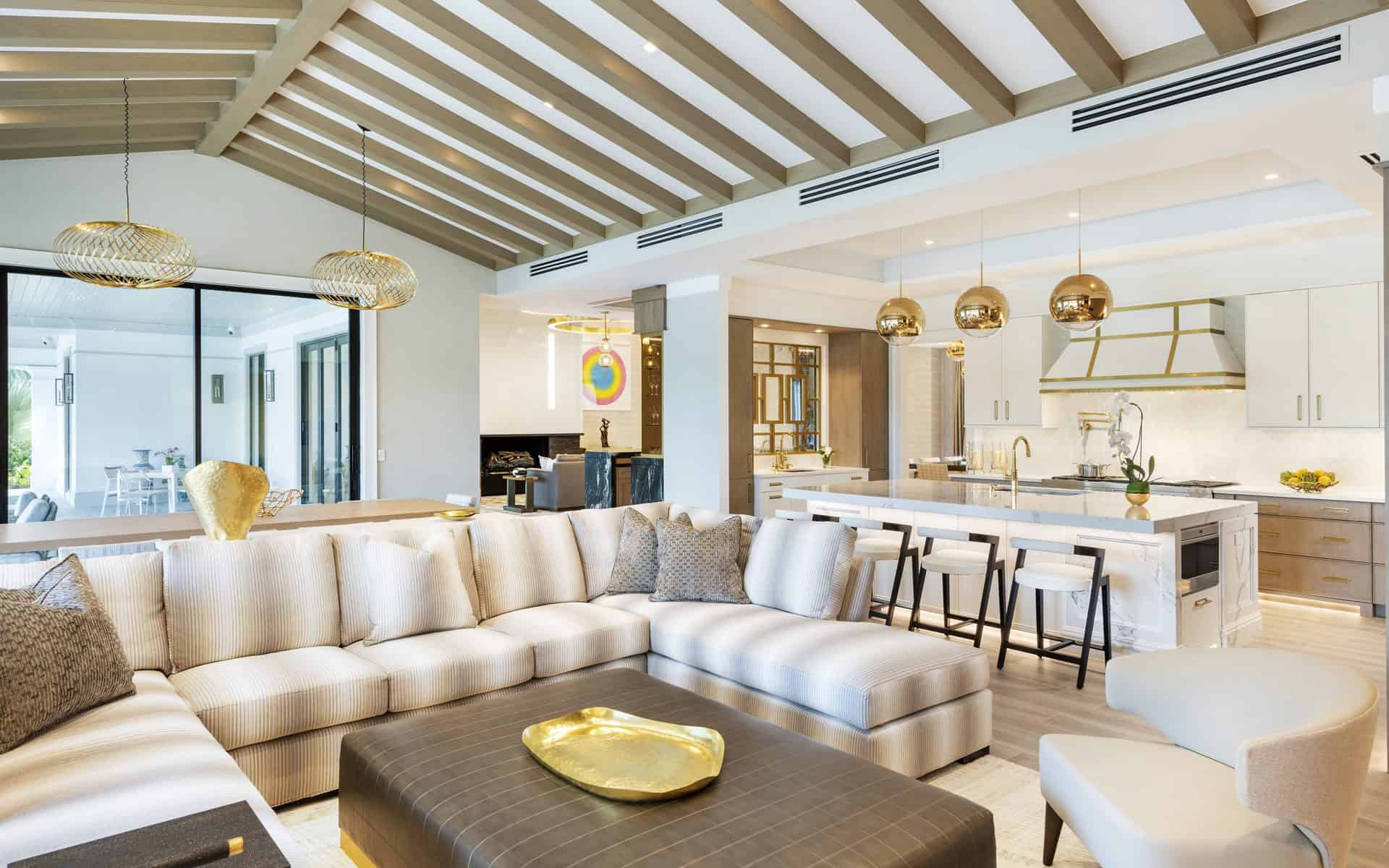 Open-concept living space features light wood beams, modern white sofas and adjacent custom white kitchen.