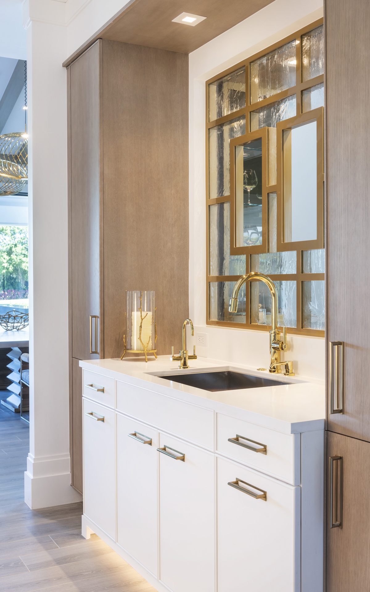 Image of contemporary bar area with white cabinetry, gold accents, and mirrored and gold backdrop.