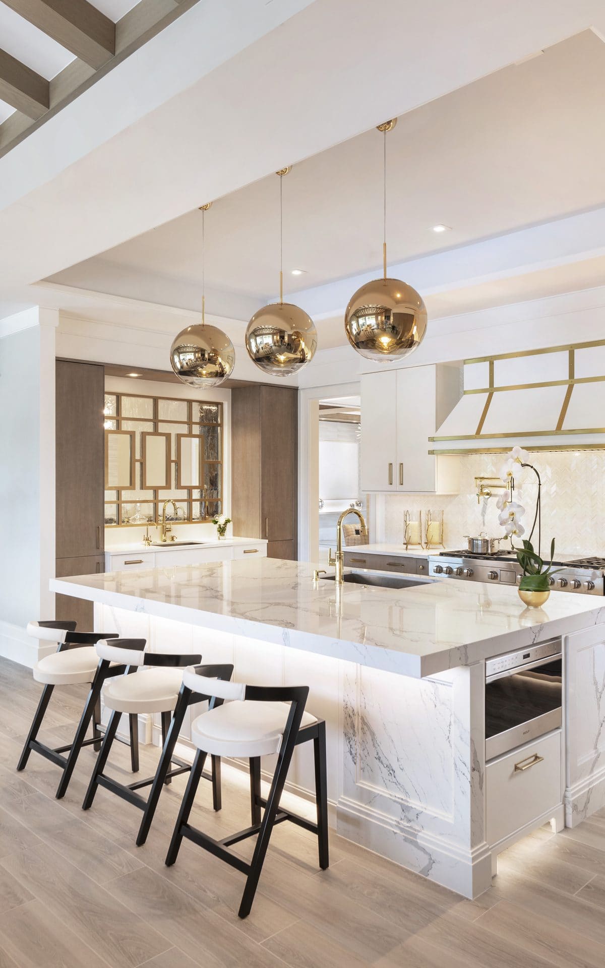 Custom Bilotta kitchen features marble island, gold pendant lights and accessories, and custom white and gold hoodvent.