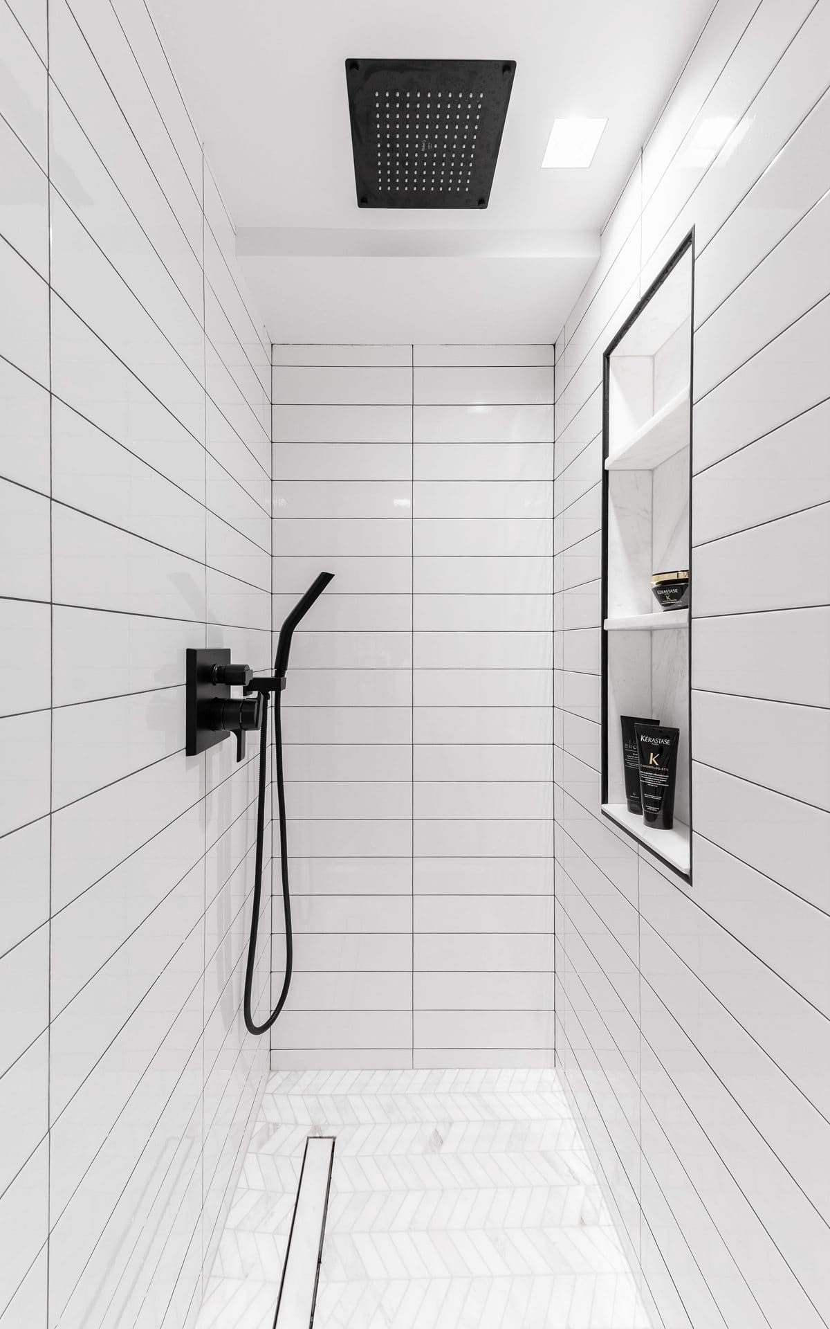 Modern custom shower features white subway tiles and dramatic black luxury fixtures and accents.