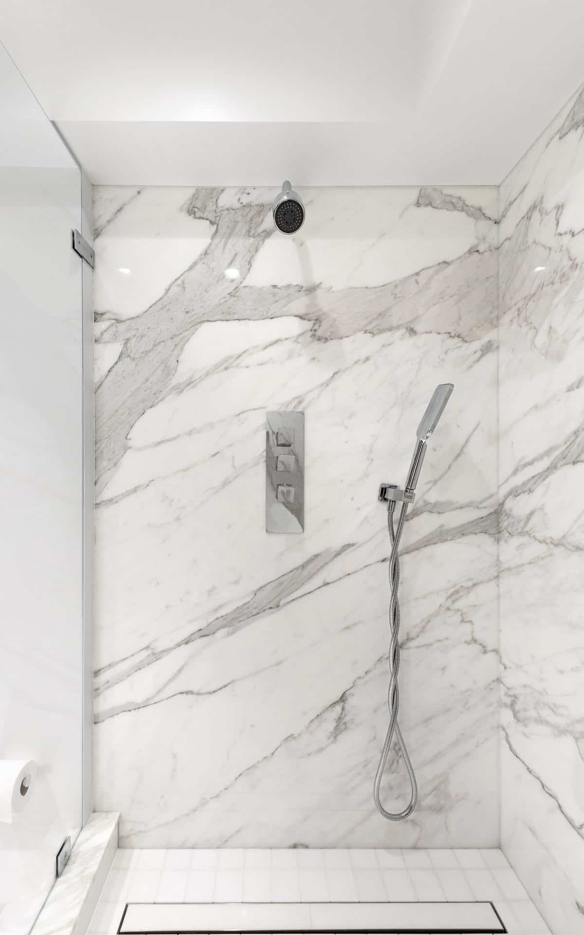 Image of modern custom shower with white and gray marble and upscale chrome fixtures.