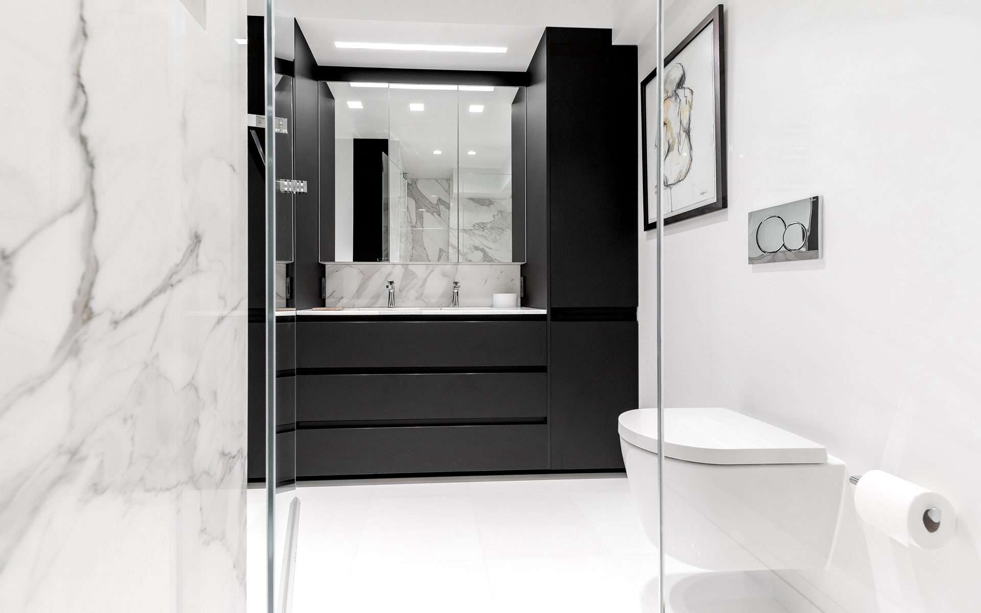 Dramatic bathroom features sleek black handle-less caninetry, marbled walls and modern bathroom appliances.