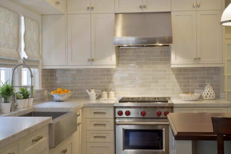 light colored kitchen with white frameless cabinetry, handmade gray porcelain tile backsplash, and Carrera marble countertops