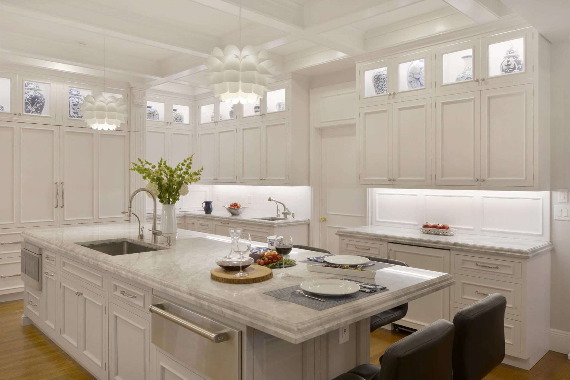 Stunning white kitchen features island that incorporates a sink, paneled dishwasher, trash pullout, microwave, and warming drawer.
