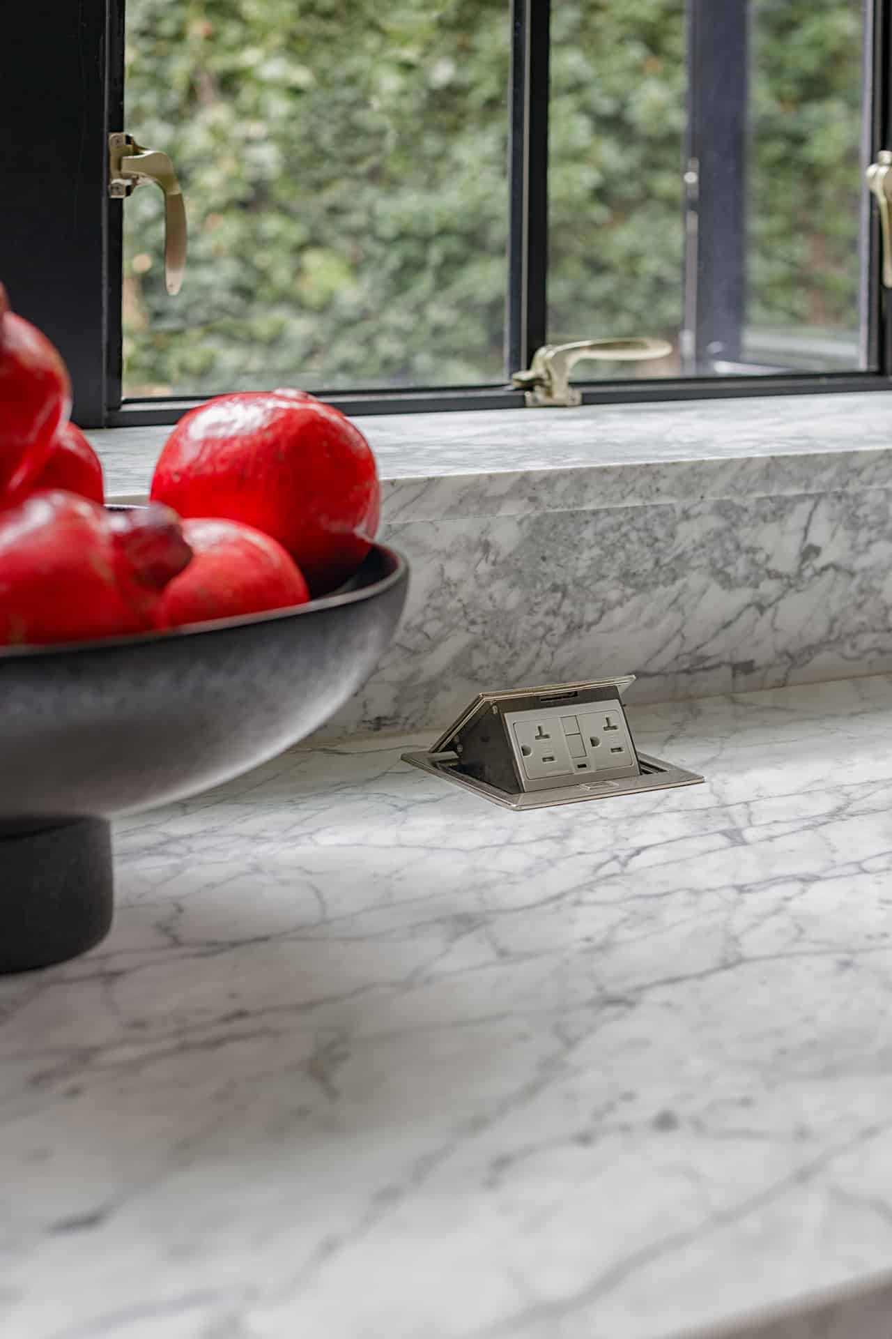 Close up of counter tops with pop up electrical outlet and bowl of pomegranates.