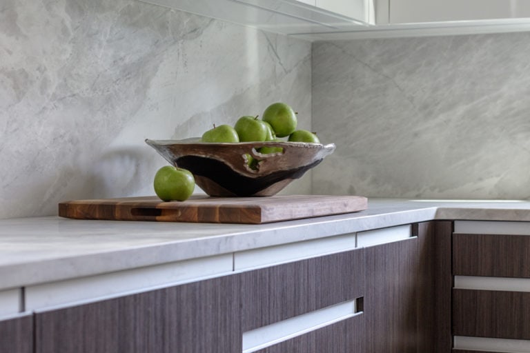 Modern bowl with green apples sitting on countertop above Artcraft cabinets open with channel hardware.