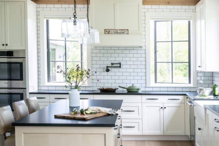 Frameless Brookhaven cabinetry with recessed doors, painted in a mix of Nordic White and Vintage Dunes with black hardware. Subway tile backsplash and farmhouse sink.
