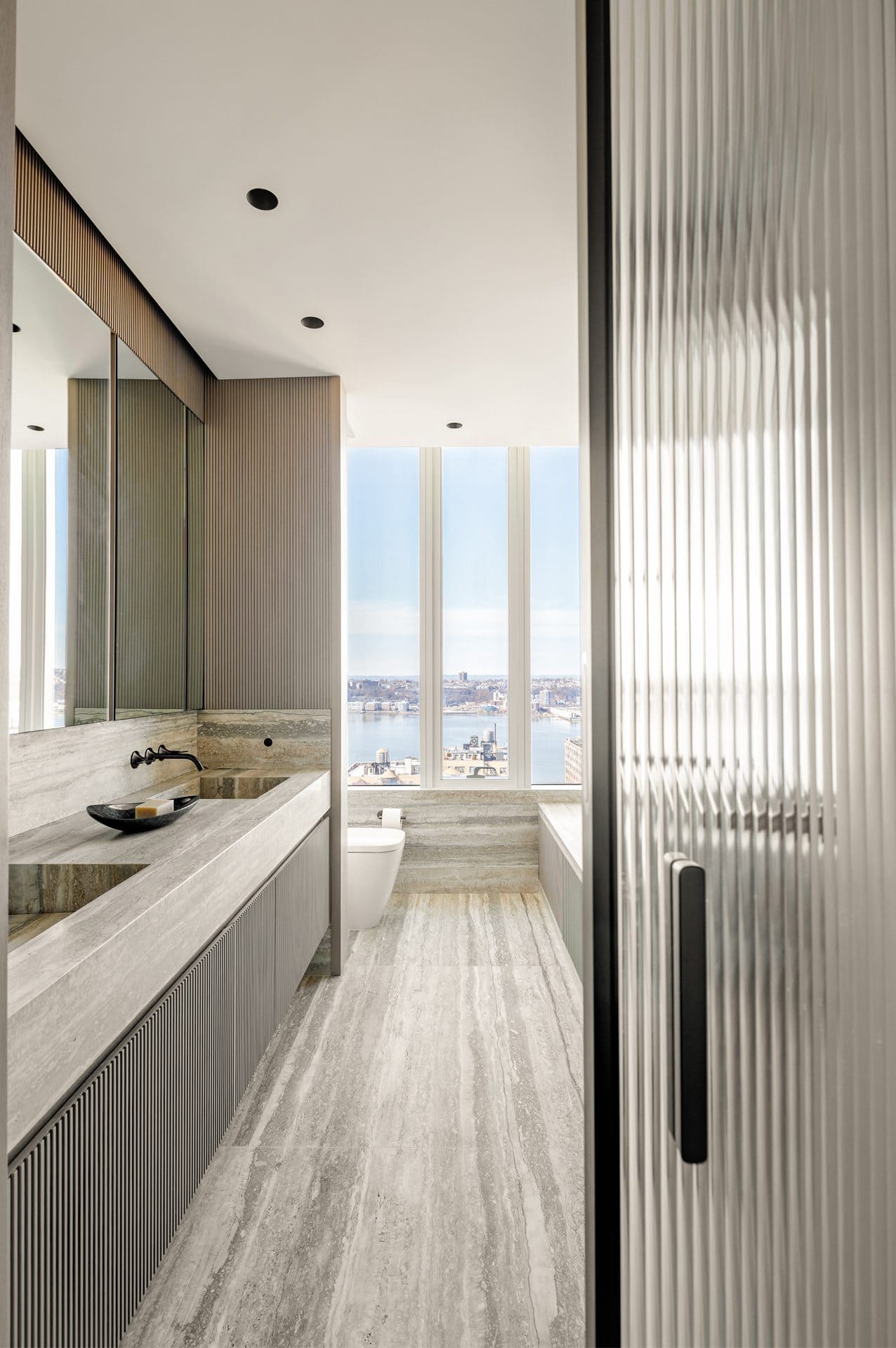 Earth-toned bathroom with Bilotta double sink vanity, pocket glass door half open and view of the Hudson River