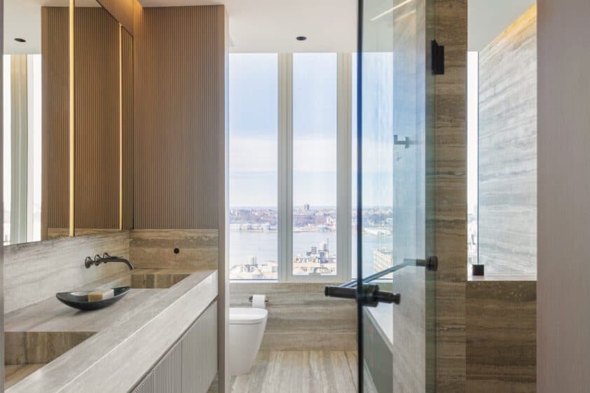 Earth-toned bathroom with Bilotta double sink vanity, shower door half open and view of the Hudson River