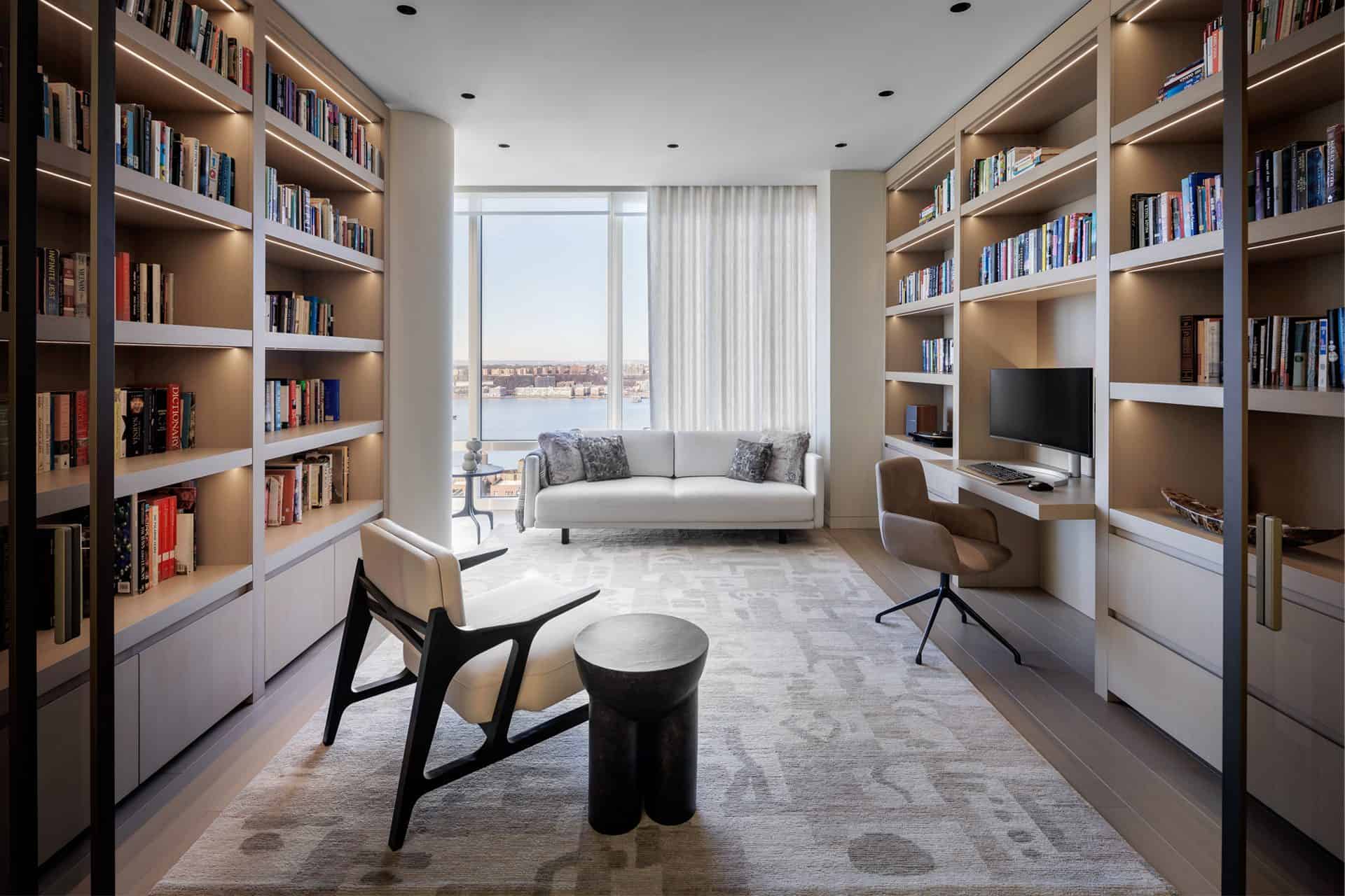 View of study of book shelves and desk area with Bilotta millwork , chair, couch and tables, with a window looking out on the Hudson River