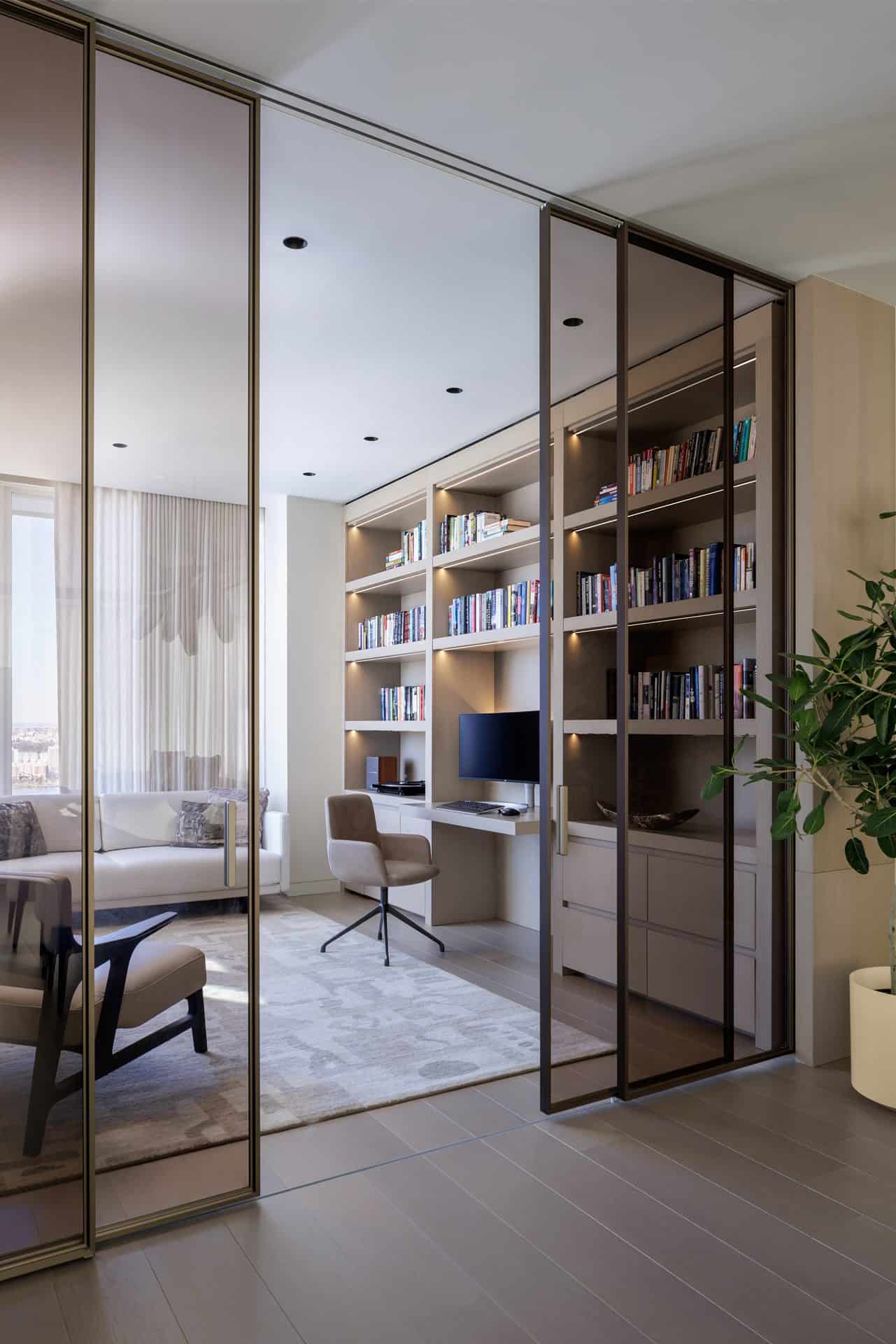 View looking through sliding glass doors of a study with book shelves and desk area with Bilotta millwork , chairs, couch and tables.