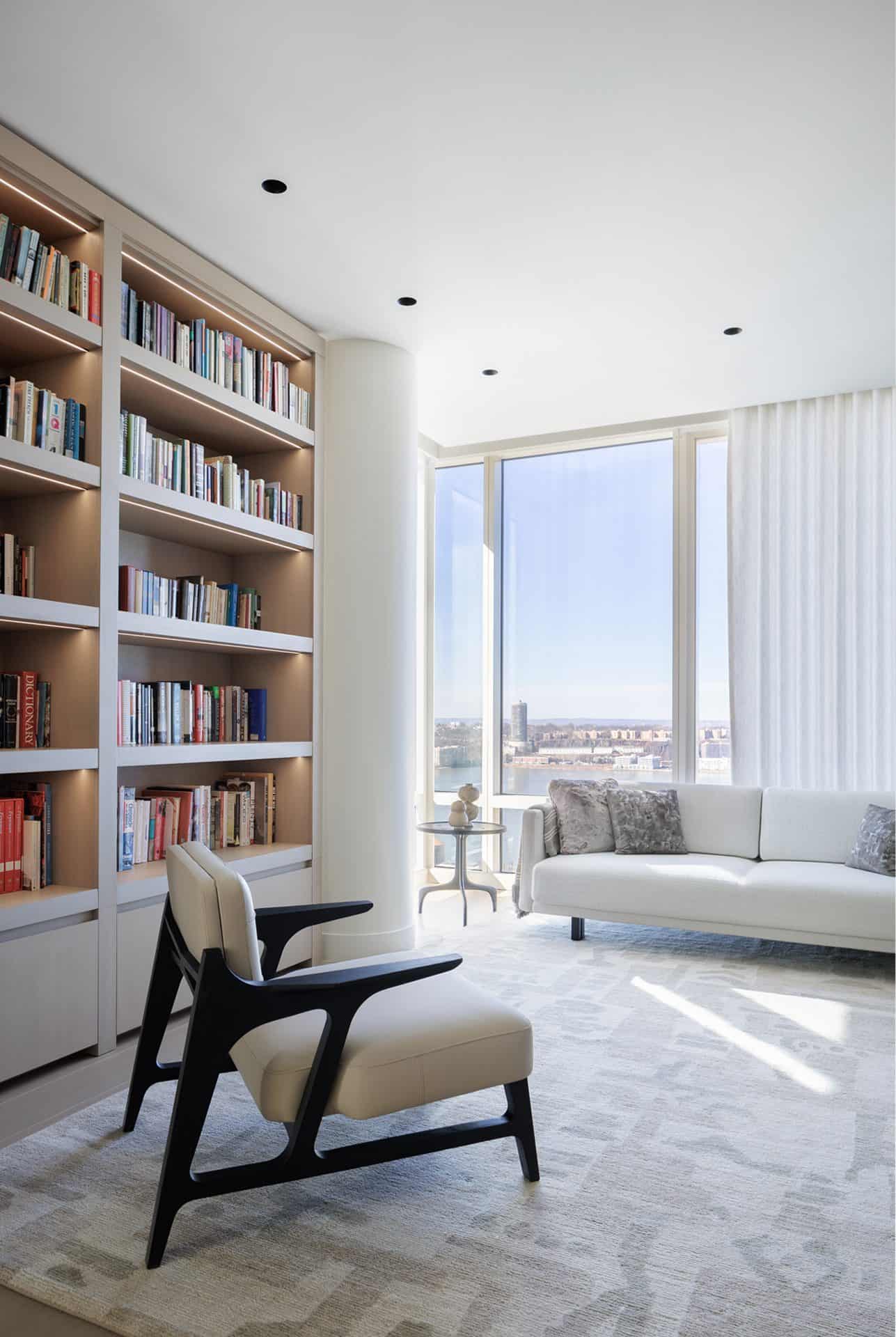 View of a study with a chair in front of book shelves Bilotta millwork, and a couch
