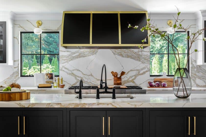 Close up of black kitchen island cabinetry with gold handles, Calacatta Gold countertops and large black and gold hood over the range