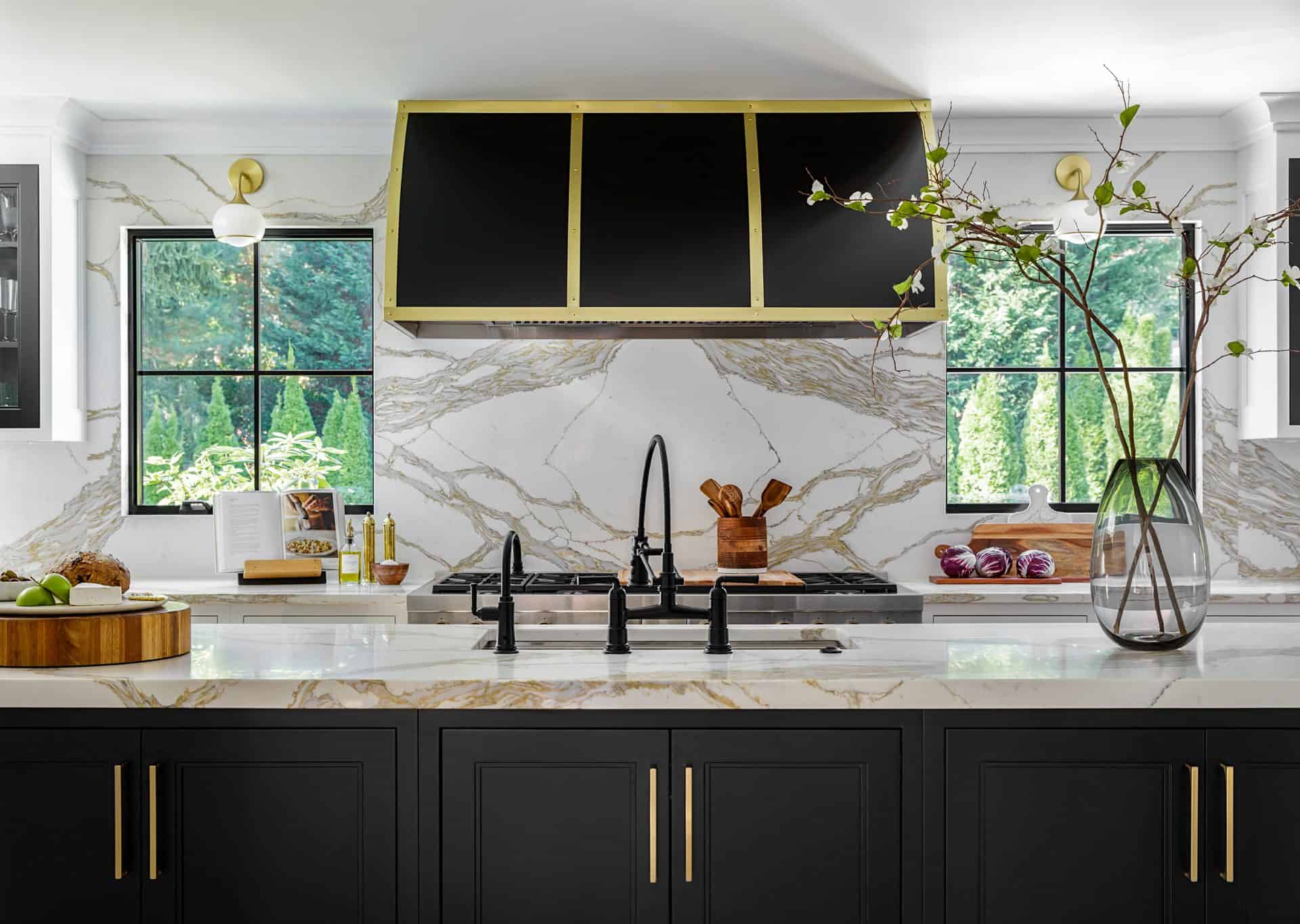 Close up of black kitchen island cabinetry with gold handles, Calacatta Gold countertops and large black and gold hood over the range