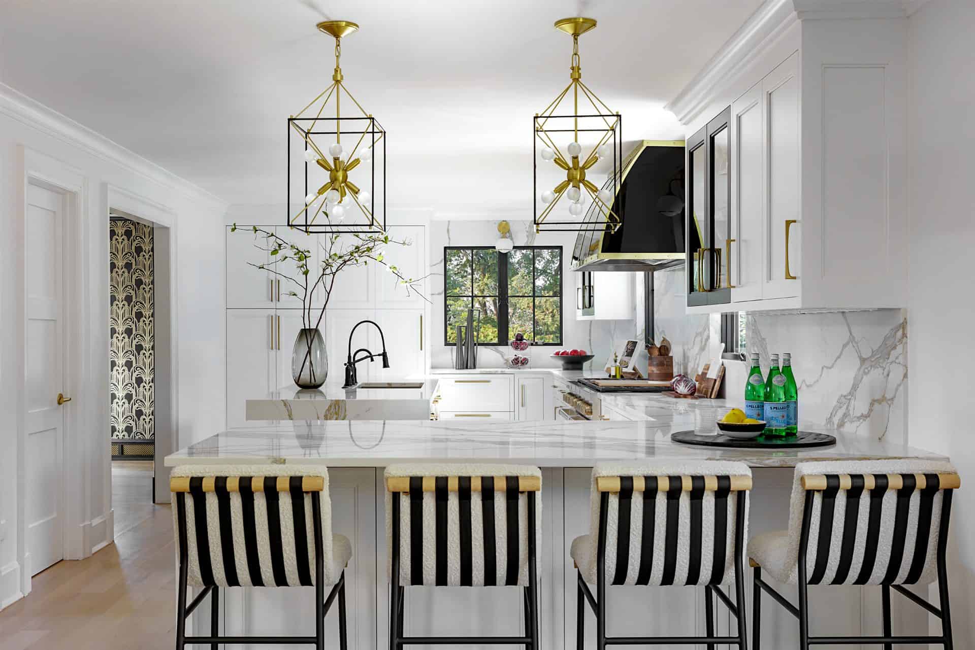 Expansive view of kitchen with four black and white stools in the foreground and geometric pendant lights above peninsula with gold accents