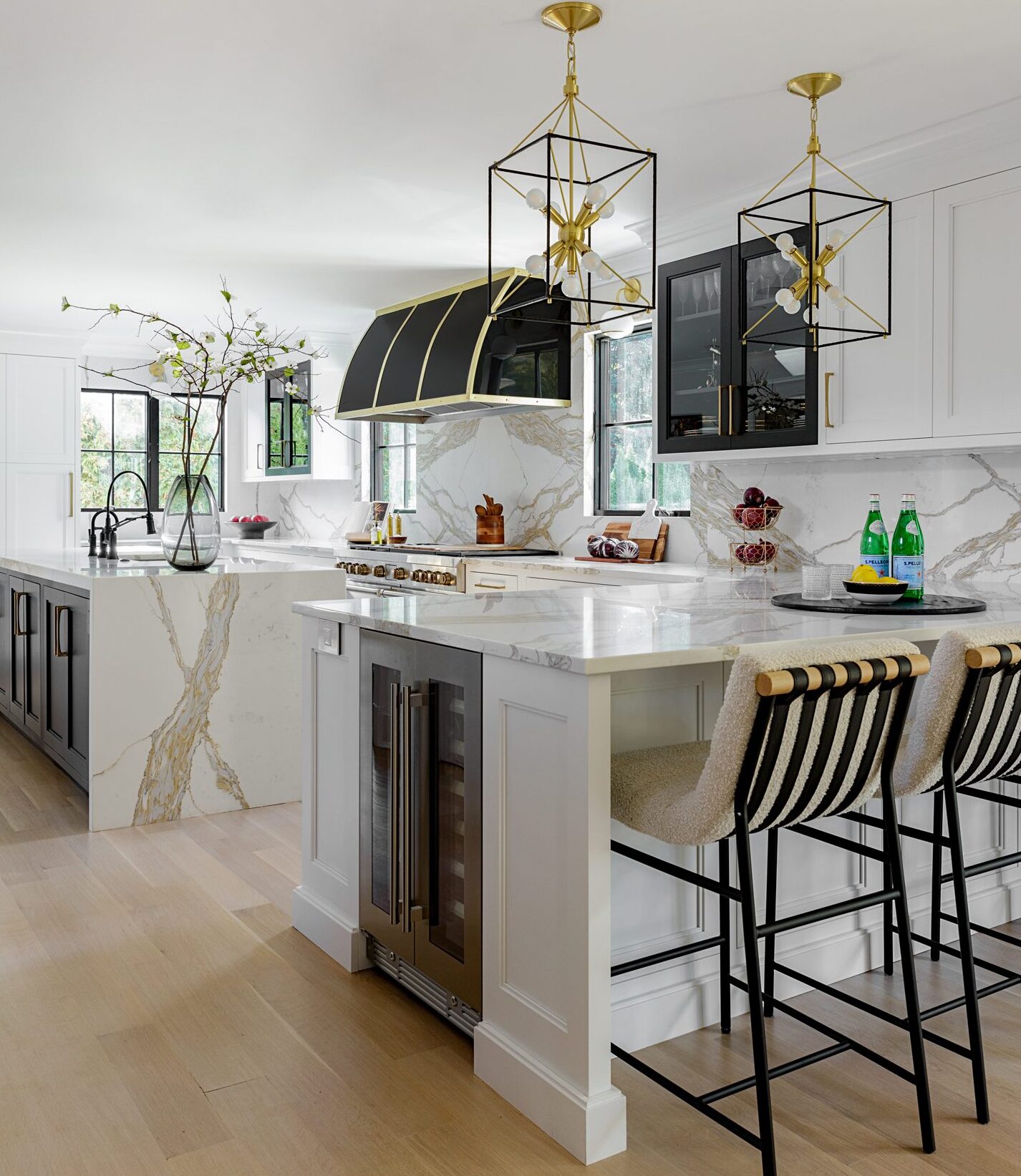 Kitchen peninsula with beverage refrigerator and island with waterfall edge, black and white cabinetry and large black and gold hood over the range