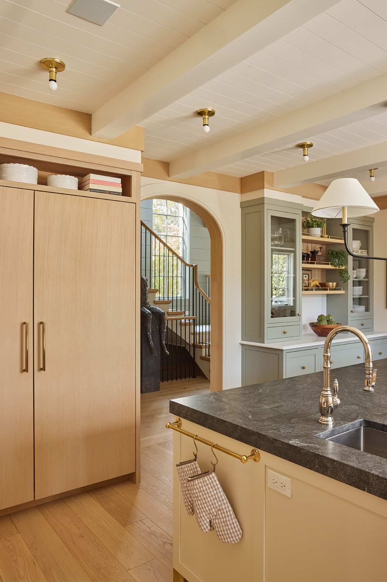 View of corner of island with prep sink, oak paneled refrigerator doors on the left, arch way in the middle, and custom hutch on the right