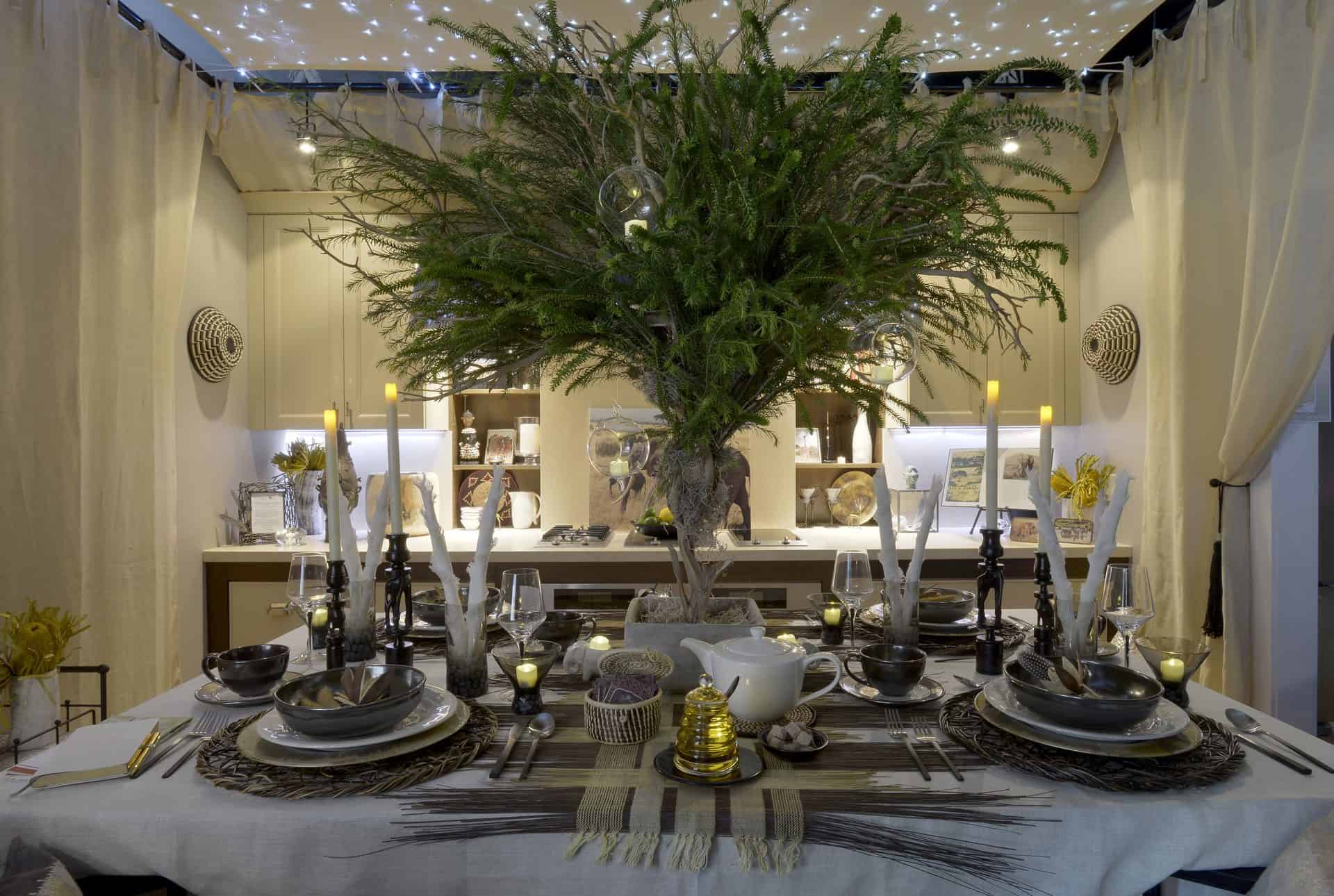 Tabletop design using browns, grays and yellows, pewter bowls and exotic accents from branch-like white candles, weaved brown and yellow straw runner and a large mixed greens cedar pine branches as centerpiece. 