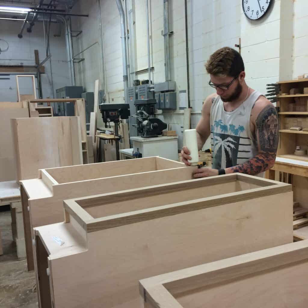 Inside a cabinet factory with a cabinet maker gluing wood cabinets together.