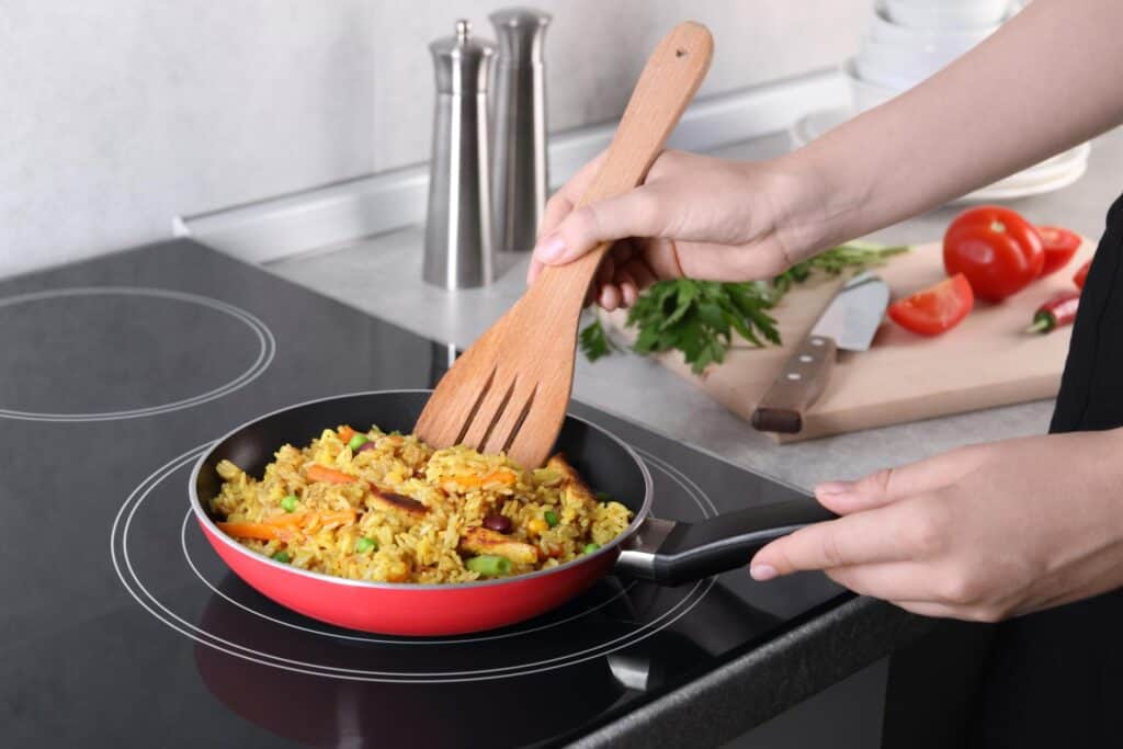 Close up of an electric range with hands cooking fried rice in a red sauté pan